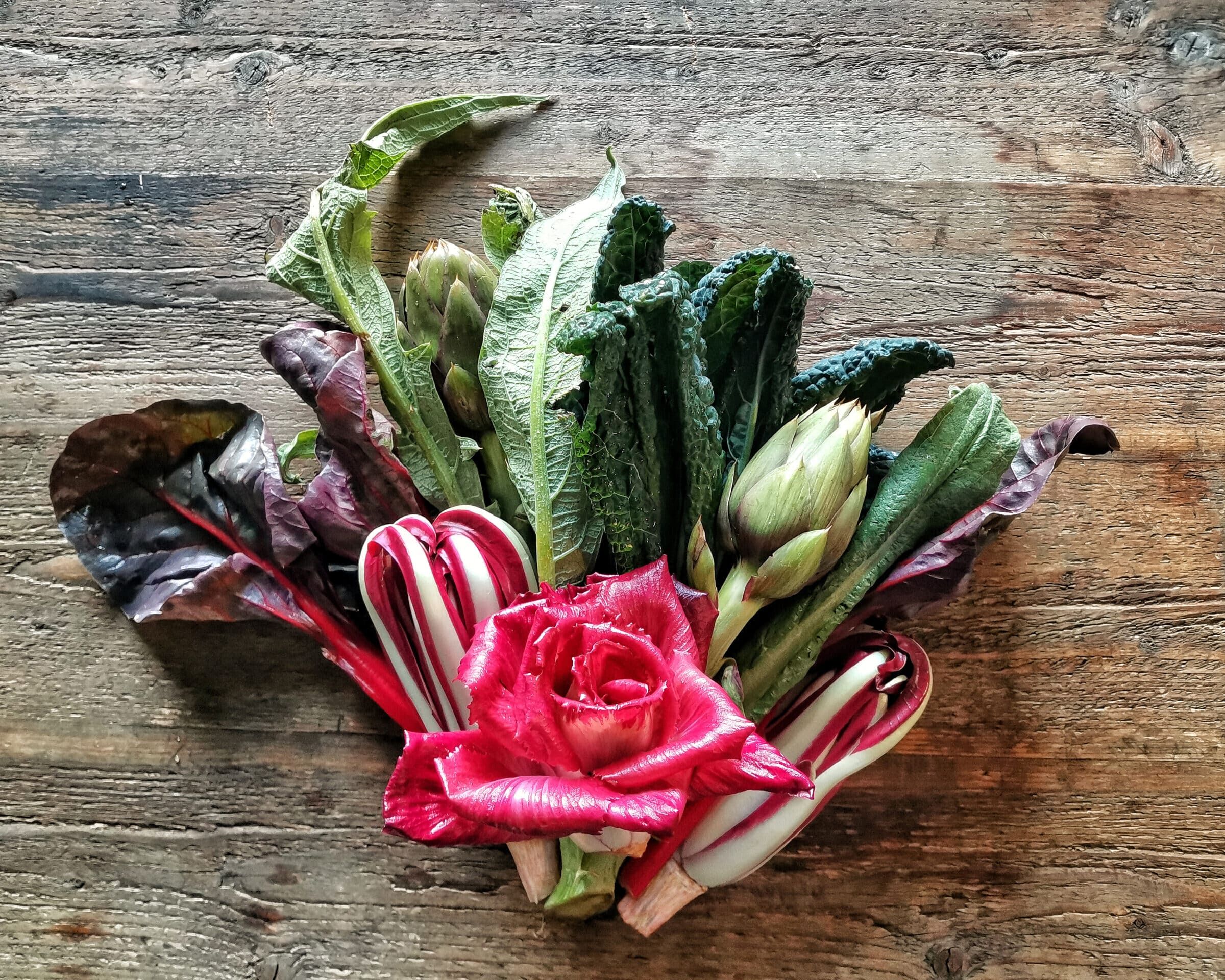 Fumagalli Danilo Ingrosso Ortofrutta Un mazzo di verdure a foglia e ortaggi assortiti, tra cui carciofi, bietole e un radicchio rosso, disposti su un vassoio di legno: l’ideale per chi è alla ricerca di prodotti ortofrutticoli di altissima qualità da Fumagalli Danilo Besana in Brianza. Ristorazione Professionale - GDO - retail - privati