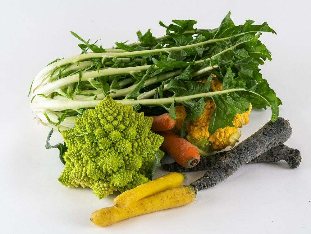 Fumagalli Danilo Ingrosso Ortofrutta Un assortimento di verdure, tra cui cicoria, broccoli romanesco, carote gialle e viola e cavolfiore provenienti dal grossista ortofrutticolo Fumagalli Danilo Besana in Brianza, disposte con cura su uno sfondo bianco. Ristorazione Professionale - GDO - retail - privati