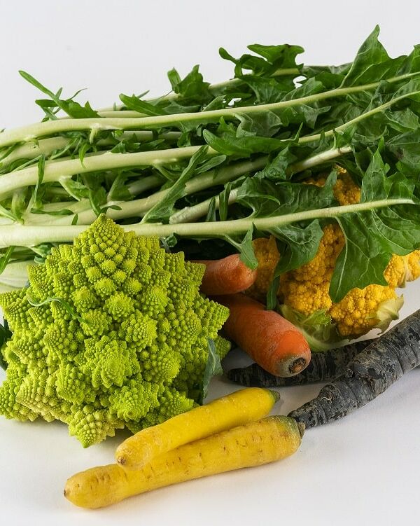 Fumagalli Danilo Ingrosso Ortofrutta Un assortimento di verdure, tra cui cicoria, broccoli romanesco, carote gialle e viola e cavolfiore provenienti dal grossista ortofrutticolo Fumagalli Danilo Besana in Brianza, disposte con cura su uno sfondo bianco. Ristorazione Professionale - GDO - retail - privati