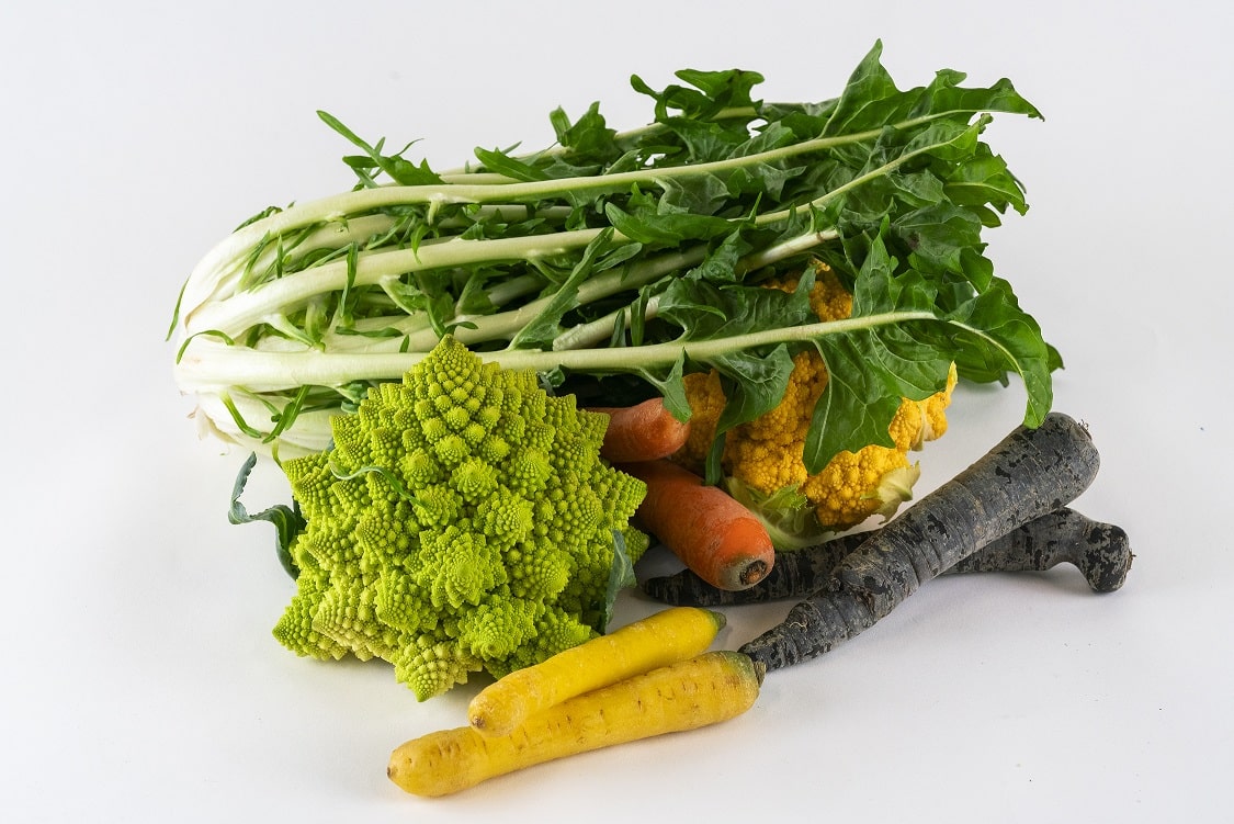 Fumagalli Danilo Ingrosso Ortofrutta Un assortimento di verdure, tra cui verdure a foglia verde, broccoli romanesco, carote gialle e arancioni, carote viola e cavolfiori gialli provenienti da Fumagalli Danilo Besana in Brianza — il vostro grossista di ortofrutta di fiducia — disposte su uno sfondo bianco. Ristorazione Professionale - GDO - retail - privati