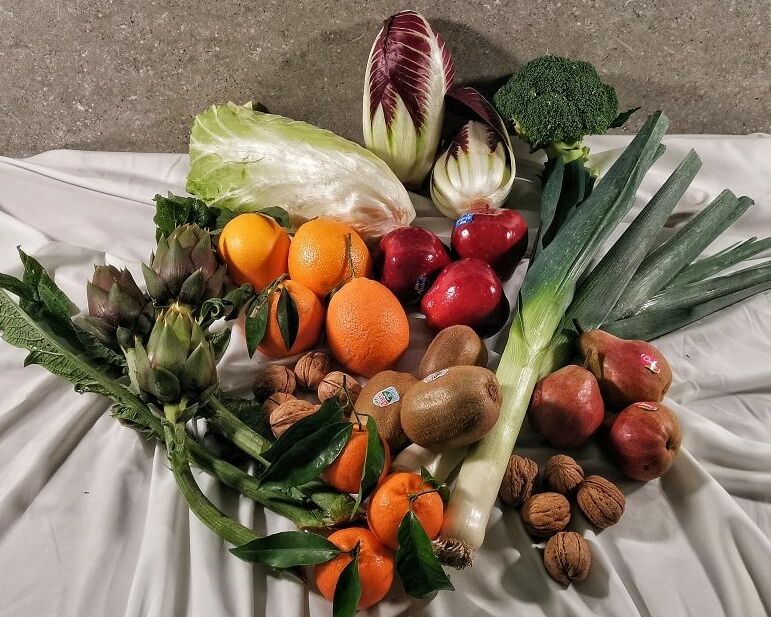 Fumagalli Danilo Ingrosso Ortofrutta Frutta fresca, verdura e frutta secca assortite — tra cui arance, mele, porri, broccoli, carciofi, indivia, pere, kiwi, mandarini, noci e lattuga — disposte su una tovaglia bianca fornita da Fumagalli Danilo Besana, grossista ortofrutta della Brianza. Ristorazione Professionale - GDO - retail - privati