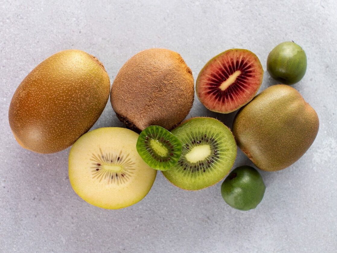 Fumagalli Danilo Ingrosso Ortofrutta Diversi kiwi interi e tagliati a met&agrave;, di diverse variet&agrave;, con la polpa verde, gialla e rossa, sono disposti su una superficie grigio chiaro da Fumagalli Danilo Besana in Brianza, uno dei principali grossisti ortofrutticoli. Ristorazione Professionale - GDO - retail - privati