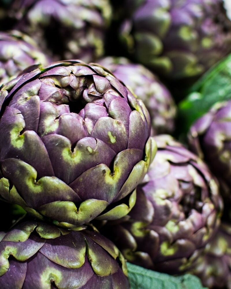 Fumagalli Danilo Ingrosso Ortofrutta Un primo piano di diversi carciofi viola freschi disposti uno sopra l’altro, provenienti da Fumagalli Danilo Besana in Brianza, che ne mette in risalto le foglie ruvide e le sfumature di verde: perfetti per la vendita all’ingrosso di frutta e verdura e per la ristorazione ortofrutticola. Ristorazione Professionale - GDO - retail - privati