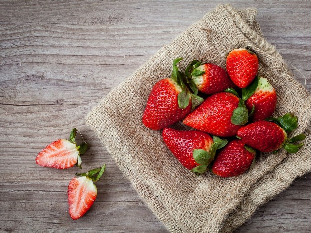 Fumagalli Danilo Ingrosso Ortofrutta Fragole fresche, alcune intere e altre affettate, giacciono su un telo di juta appoggiato su un piano di legno, a testimonianza della qualità selezionata da Fumagalli Danilo Besana in Brianza per il settore ortofrutticolo della ristorazione. Ristorazione Professionale - GDO - retail - privati