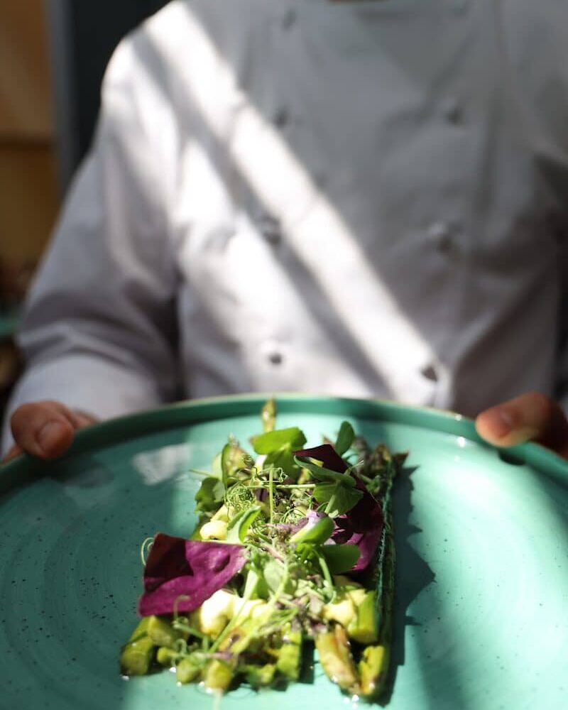 Fumagalli Danilo Ingrosso Ortofrutta Uno chef in camice bianco tiene in mano un piatto verde con una porzione rettangolare di verdure, elegantemente guarnita con insalata mista e microverdure, che mette in risalto la qualità degli ingredienti provenienti da Fumagalli Danilo Besana in Brianza, un nome di fiducia nel settore della vendita all’ingrosso di frutta e verdura per la ristorazione. Ristorazione Professionale - GDO - retail - privati
