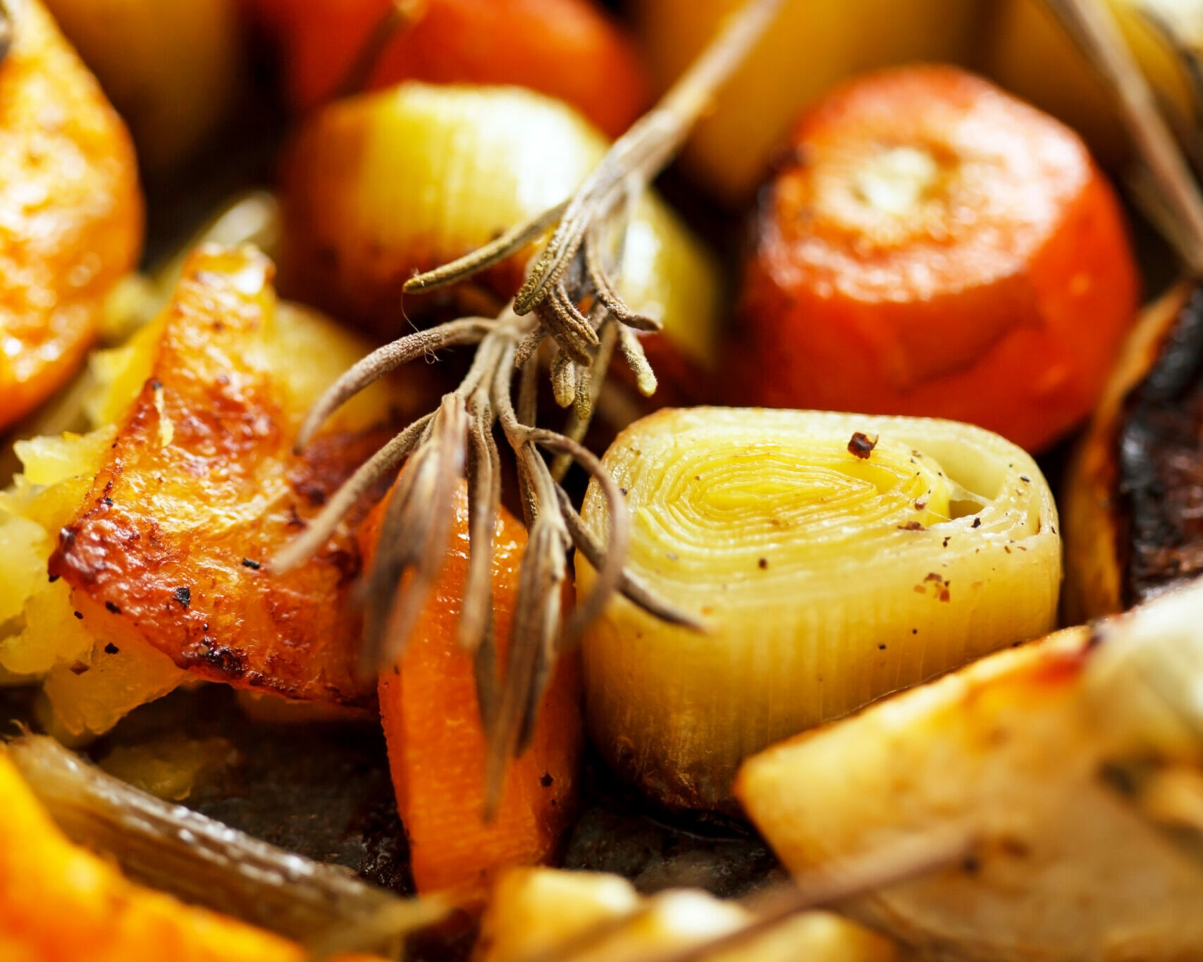 Fumagalli Danilo Ingrosso Ortofrutta Primo piano di ortaggi a radice arrostiti, tra cui carote, porri e patate, guarniti con rametti di rosmarino fresco: perfetti per la ristorazione “ortofrutta” di Fumagalli Danilo Besana in Brianza. Ristorazione Professionale - GDO - retail - privati