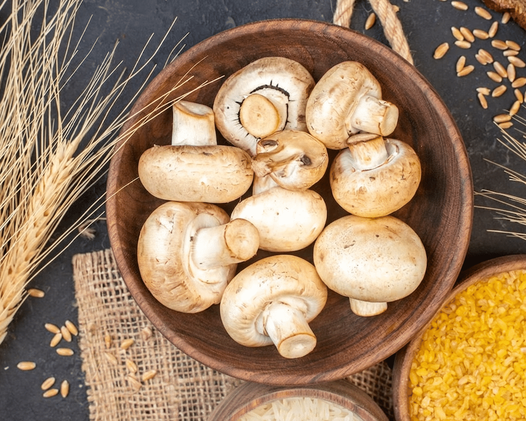 Fumagalli Danilo Ingrosso Ortofrutta Una ciotola di legno piena di funghi bianchi interi è adagiata accanto a steli di grano, chicchi e una ciotola di bulgur giallo su una superficie scura: l’allestimento perfetto per mettere in risalto gli ingredienti freschi forniti da Fumagalli Danilo Besana in Brianza, uno dei principali grossisti ortofrutticoli per il settore della ristorazione. Ristorazione Professionale - GDO - retail - privati